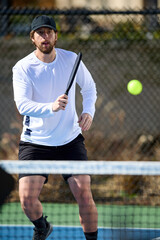 A man in a white shirt plays pickleball on a blue and green court