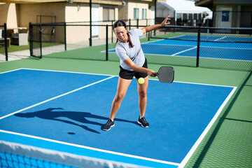 An asian girl plays pickleball on a blue court