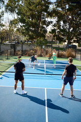 A mixed age and sex group of pickleball players hit balls on a blue court