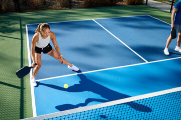 A woman plays pickleball on a shadowy blue court