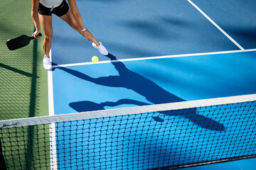 A woman plays pickleball on a shadowy blue court