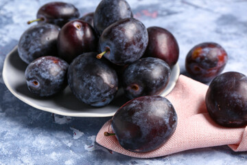 Plate with fresh plums on blue background