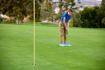 Obraz premium A young girl putts a golf ball on a golf course at dusk
