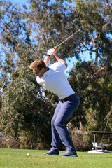 A male golfer in his backswing on a golf course with trees behind