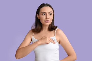 Young woman checking her breast on lilac background. Cancer awareness concept