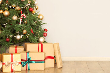 Glowing Christmas tree with presents near light wall in room