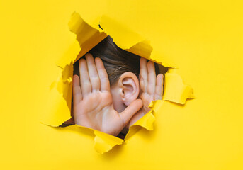 Female ear and hands close-up. Copy space. Torn paper, yellow background. The concept of...