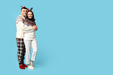 Fototapeta premium Happy young couple in Christmas pajamas hugging on blue background