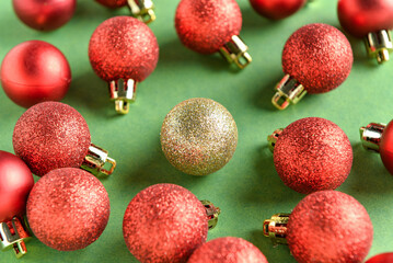 One golden Christmas ball among red ones on green background. Concept of uniqueness
