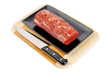 A beef tenderloin center cut roast on a black plate with a large butcher knife isolated on white