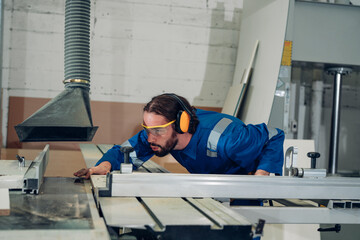 Skilled carpenter cutting a piece of wood in his woodwork workshop, and wearing safety googles and...