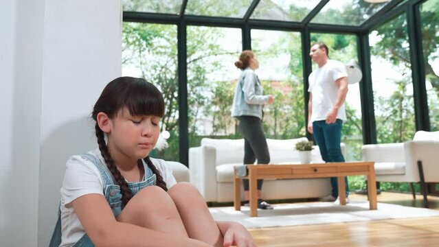 Stressed and unhappy young girl huddle in corner, cover her ears blocking sound of her parent arguing in background. Domestic violence at home and traumatic childhood develop to depression. Fastidious