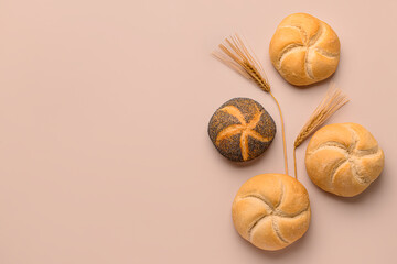 Delicious kaiser rolls and wheat ears on beige background