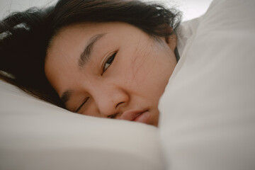Close up of asian Thai woman closing eyes, sleeping on white bed with white blanket covering in the morning at room apartment. 
