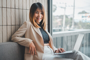 Cheerful businesswoman working on her laptop, comfortably lounging in a sunlit office space,...