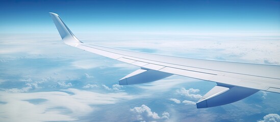 Obraz premium An aerial shot capturing a commercial jet planes wing above fluffy clouds with the Pacific Ocean visible below. The wing is turning upwards on the left side of the frame.