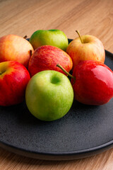 delicious apples on a plate on a wooden table, bitten apple, red apple and green apple