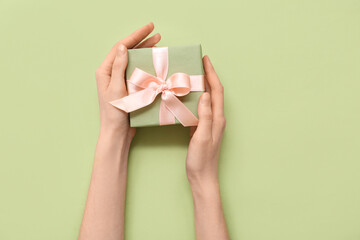 Female hands with gift box on green background. International Women's Day