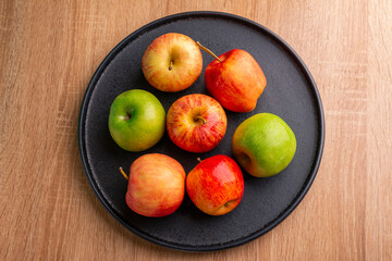 delicious apples on a plate on a wooden table, bitten apple, red apple and green apple