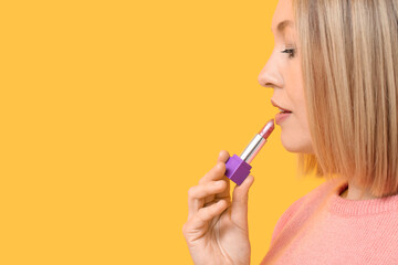 Woman applying lipstick against yellow background