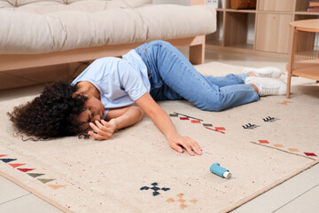 Young African-American woman with asthma inhaler lying on floor at home