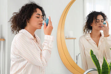 Young African-American woman using asthma inhaler in bathroom - obrazy, fototapety, plakaty