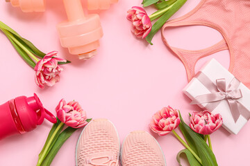 Frame made of dumbbells, shoes, clothes and tulip flowers on pink background. International Women's Day
