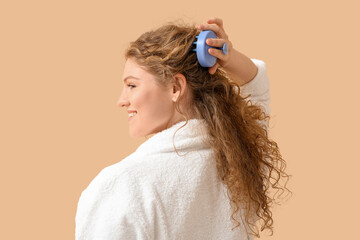 Beautiful young woman using hair scalp massager on beige background