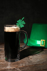 Mug of dark beer with leprechaun hat and clover for St. Patrick's Day celebration on wooden table...