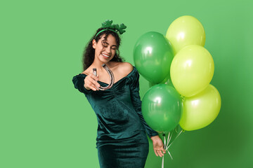 Beautiful young African-American woman with air balloons and horseshoe on green background. St....