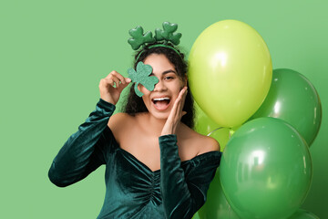 Beautiful young African-American woman with clover and air balloons on green background. St....