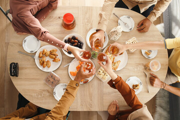 Hands of people holding glass of tea and a table full with iftar food, top view