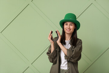 Beautiful young woman in leprechaun hat with horseshoe on green background. St. Patrick's Day...