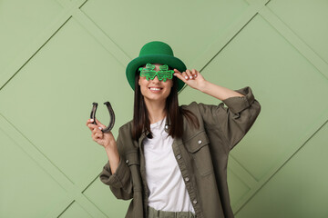 Beautiful young woman in leprechaun hat with horseshoe on green background. St. Patrick's Day...