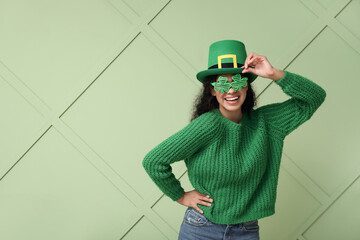 Beautiful young African-American woman in leprechaun hat and decorative glasses on green...