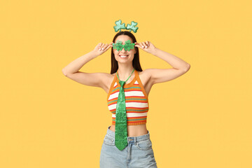 Beautiful young woman in headband and decorative glasses on yellow background. St. Patrick's Day...