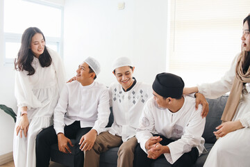 Young Asian muslim friends, man and woman, sitting, talking and laughing together during Ramadan or Eid mubarak celebration - obrazy, fototapety, plakaty