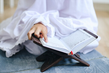 Hands of muslim girl reading quran while sitting on prayer mat