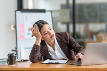Fototapeta premium Stressed asian businesswoman with headache working at laptop in office. Stress and health at work concept.