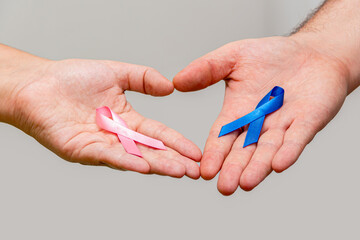 Two hands holding two Pink and Blue ribbons for the Pink October and Blue November campaigns to support life and raise awareness about cancer. Man's hand and woman's hand