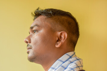 Obraz premium Side view of a young Indian man isolated on a yellow background with a fresh hairstyle. Barbershop photo of a client after a haircut.