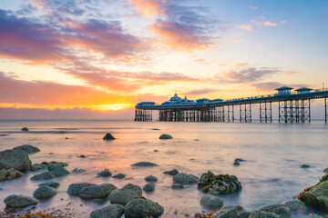 Vibrant colorful sunrise over the rugged rocky coastline with Llandudno Pier in the background -...