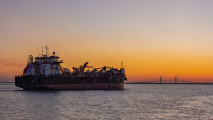 Fototapeta premium cargo ship sailing in to dock with a suspension bridge off in the distance in St. Simons, GA
