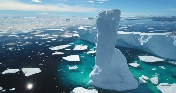 Towering melting iceberg in Arctic icy ocean. Snow covered glacier drift under blue sunny sky. Pure ice floats in turquoise water. Ecology, melting ice, climate change global warming. Aerial view