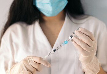 nurse with face mask injecting vaccine into a syringe