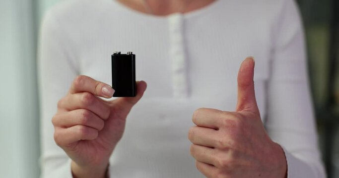 Closeup of a hand holding a black battery and showing thumbs up