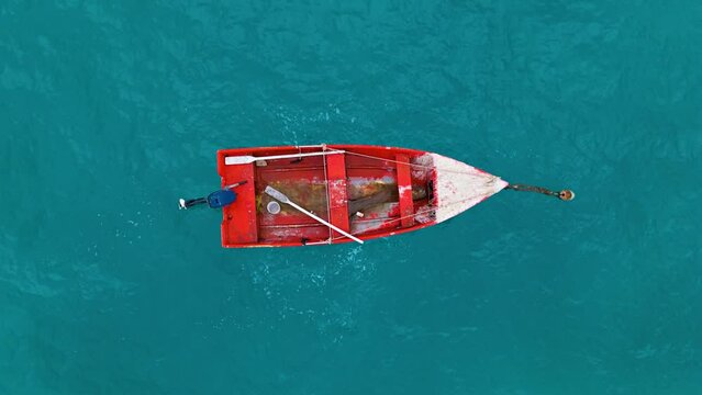 Old Red wooden boat with dirty water tethered to buoy with paint chipping and oars left inside, aerial top down overview