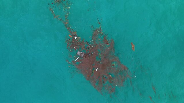 Drone bird's eye view rotate ascend above trash marine debris floatsam patch in middle of ocean water