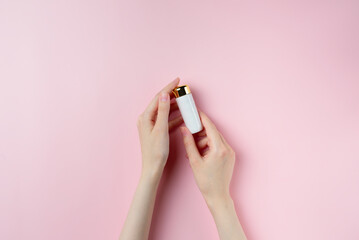 Woman's hands holding a small white tube on pastel pink background