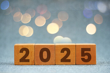 Wooden cube with engraved number 2025 on table with bokeh background